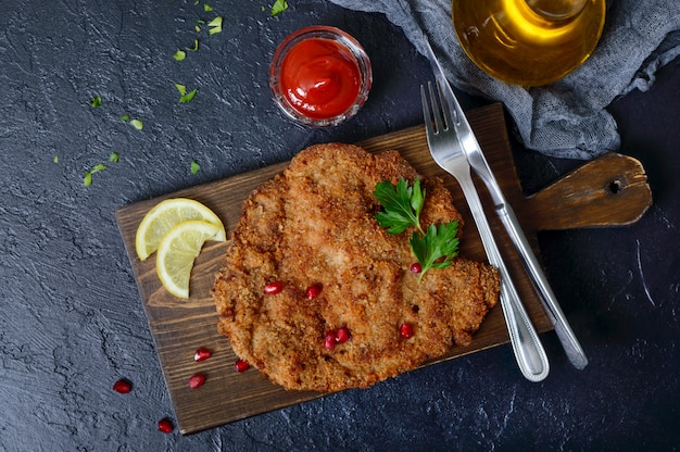 Grote weense schnitzel op een zwart oppervlak. vleesschotel. bovenaanzicht, plat lag.