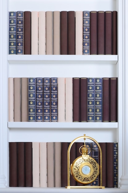 Grote witte boekenplank met veel boeken van verschillende kleuren en gouden klok