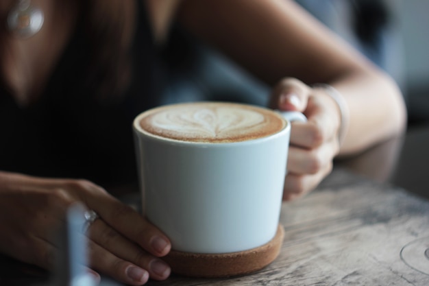 Grote witte kop met cappuccino in vrouwelijke handen, selectieve aandacht