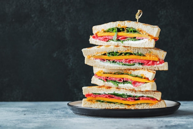 Grote zelfgemaakte sandwich met worstkaas en rucola op een donkere betonnen achtergrond