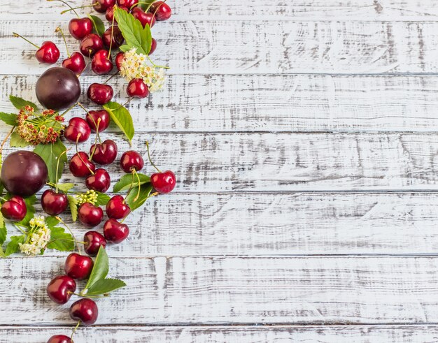 Grote zoete sappige kersen, pruimen en druiven, gebladerte en bloemen op een houten achtergrond