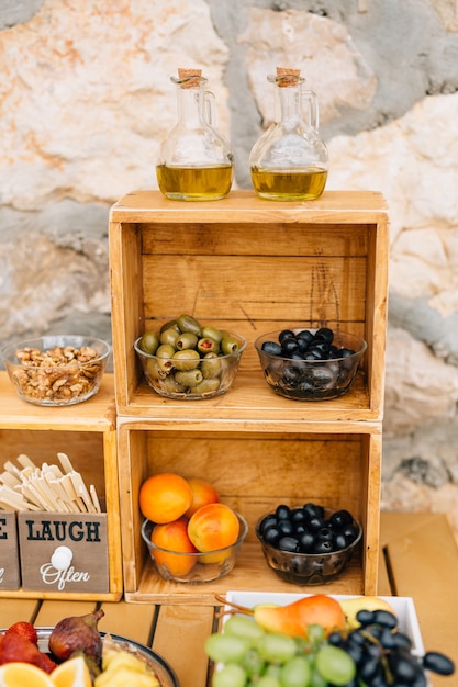 Grote zwarte en groene olijven in glazen slakommen en twee glazen kannen voor olijfolie op een houten standaard