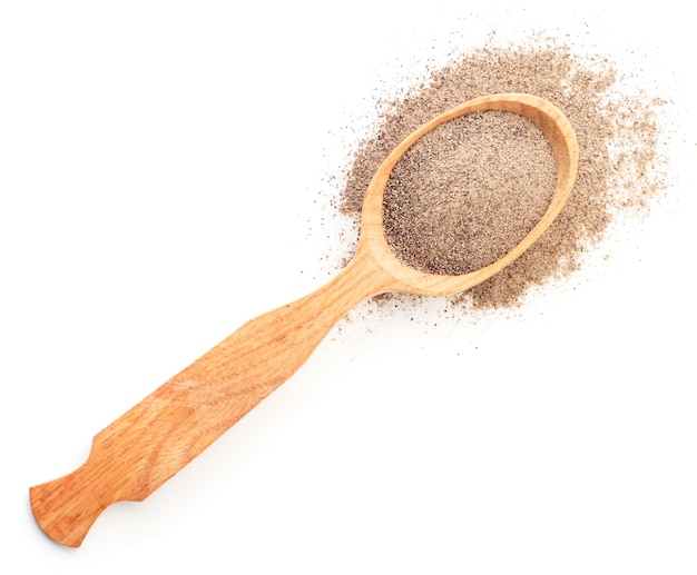 Ground black pepper in a wooden spoon close-up on a white background. Top view