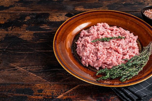 Ground chicken or turkey meat, raw Poultry on rustic plate with herbs. Dark background. Top View. Copy space.