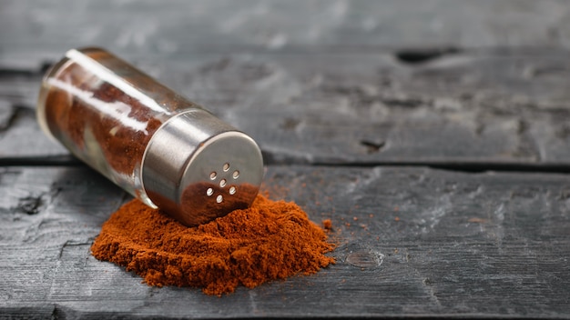 Ground chili is poured from a jar on a dark wooden table