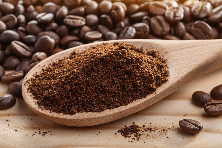 Ground coffee in spoon next to coffee beans
