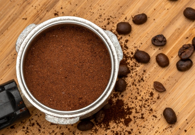 Ground and compressed coffee in the filter holder with coffee beans scattered around