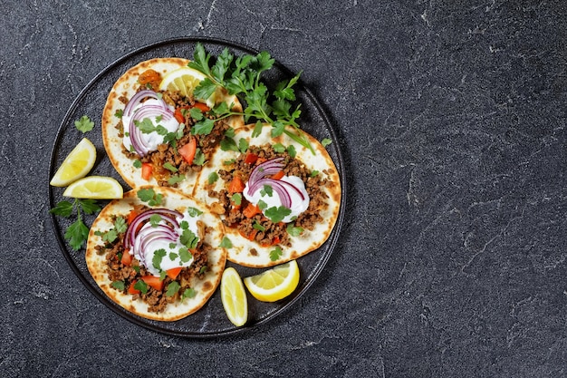 Ground Lamb Flatbreads topped with yogurt, coriander leaves and red onion on a black platter on a concrete table, top view, flat lay, free space