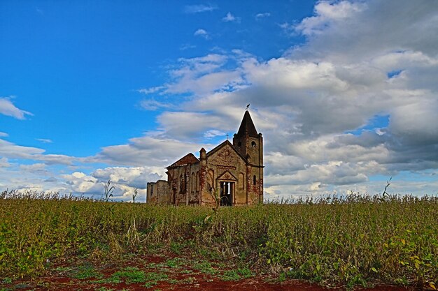 Ground level of abandoned stone church located in green grassy field against cloudy blue sky in pal