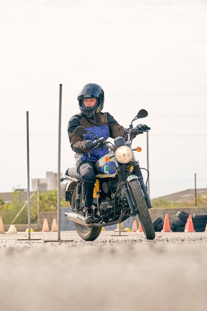 Ground level of female motorcyclist riding motorbike on asphalt motordrome with metal obstacles and oranges cones
