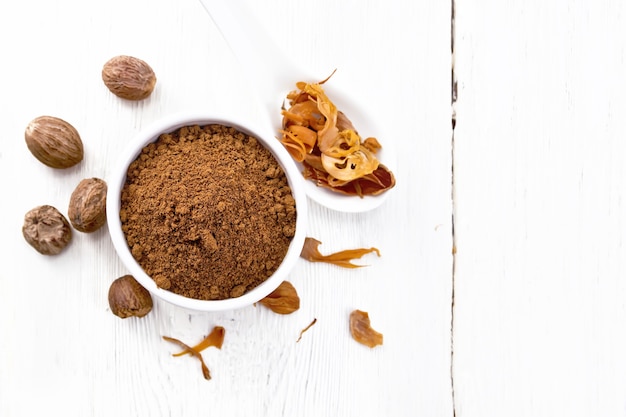 Photo ground nutmeg in a bowl and dried nutmeg arillus in a spoon, whole nuts on wooden board background from above