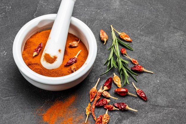 Ground paprika in ceramic mortar and pestle. Dry pepper pods on the table. Top view. Black background.