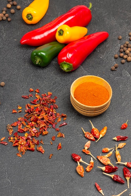 Ground pepper in wooden bowl. Raw, red pepper, dry pepper pods on table. Flat lay. Black background