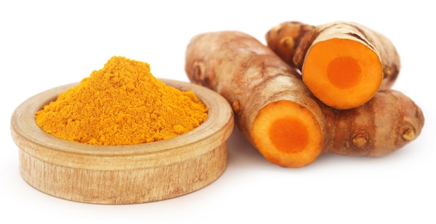 Ground and raw turmeric over white background