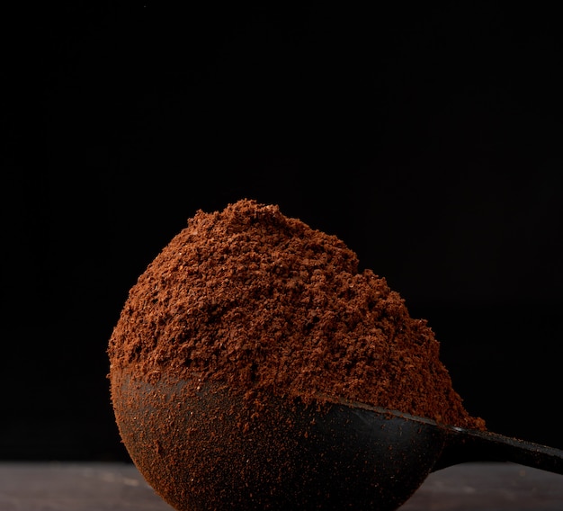 Ground roasted coffee arabica in a spoon on a black background