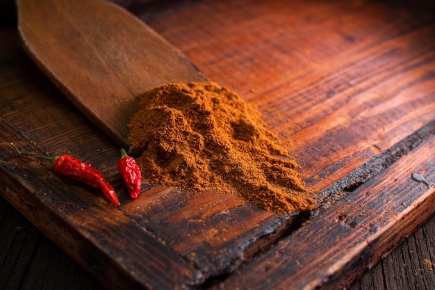 Ground seasoning and spices with spicy dried red chili peppers on a wooden board in a dark background