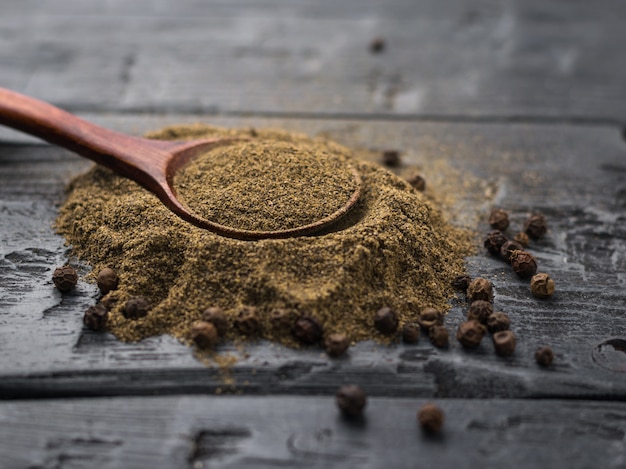 Ground and a whole black pepper is poured from a wooden spoon on the table.