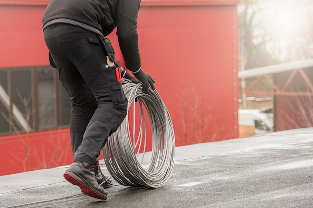 Ground wire a worker lays a ground cable on the roof of a building electrician fixing aluminum wire