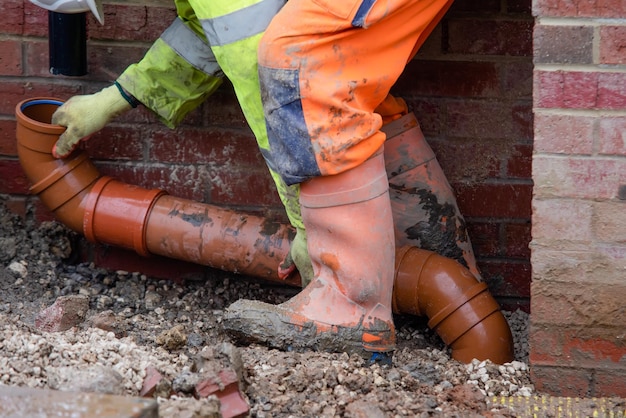 Groundworker fitting plastic drainage pipe to connect rain water pipe on new build house