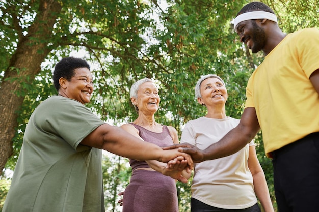 Group of active senior women stacking hands with trainer after outdoor workout