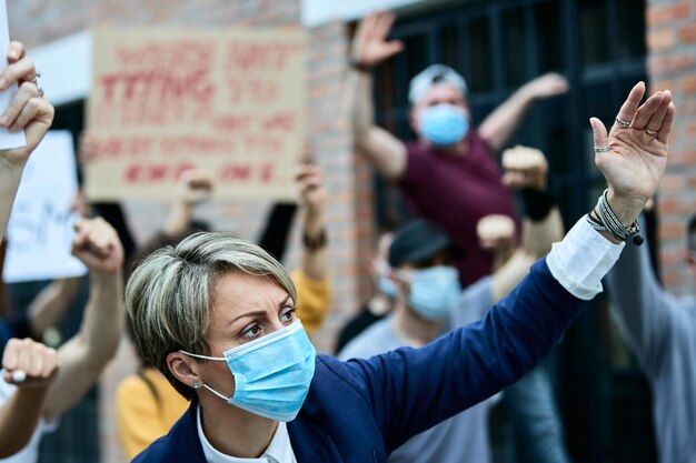 Group of activists on street demonstrations during coronavirus pandemic Focus is on businesswoman wearing protective face mask