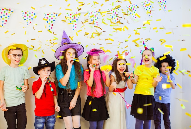Group of adorable kids having fun at birthday party Happy friends blowing whistles Children enjoying festive confetti