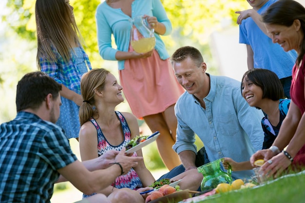 A group of adults and children sitting on the grass under the shade of a tree A family party