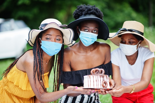 Gruppo di ragazze afroamericane con maschere facciali che celebrano la festa di compleanno all'aperto con decorazioni durante la pandemia di coronavirus.