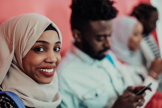 Photo a group of african muslim students using smartphones while standing in front of a pink background. high-quality photo