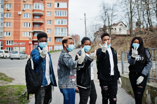 医療マスクを身に着けている建物と空の通りに対するアフリカのティーンエイジャーの友人のグループは、コロナウイルスウイルス検疫から感染や病気から保護します。