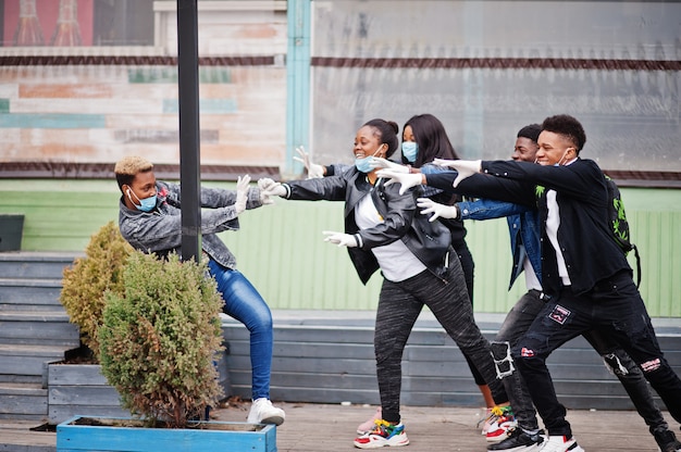 Gruppo di amici adolescenti africani al parco che indossano maschere mediche proteggono da infezioni e malattie quarantena del virus coronavirus.