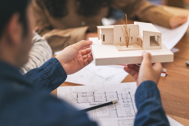 Group of an architect holding and discussing about an architecture model with shop drawing paper on table in office