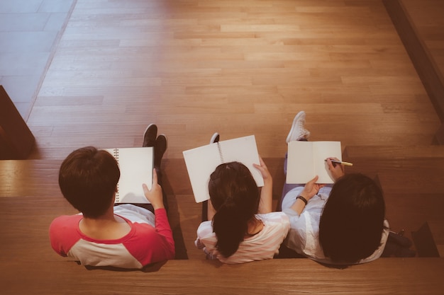 Group of asia students holding blank notebooks while sitting on stair library with copy space in vintage tone, education and people concept background