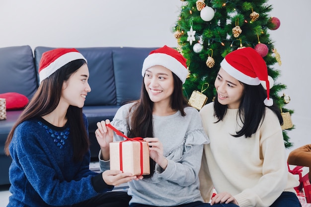 ギフト用の箱を保持しているアジアの美しい女性のグループ。休日のクリスマスツリーの装飾が付いている部屋で笑顔