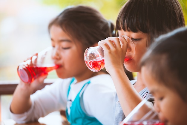 유리에서 얼음과 붉은 주스 물을 함께 마시는 아시아 어린이의 그룹