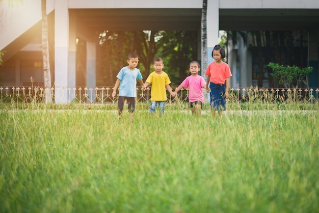 Group of asian children holding hands and running or walking together on grass field at school