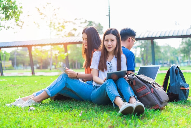 Gruppo di studenti universitari asiatici utilizzando tablet e laptop sul campo di erba all'aperto