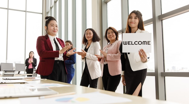 Group of Asian female  businesspeople joins together greeting and hold welcome words for a sign of happiness and pleasure for coming of something or someone.