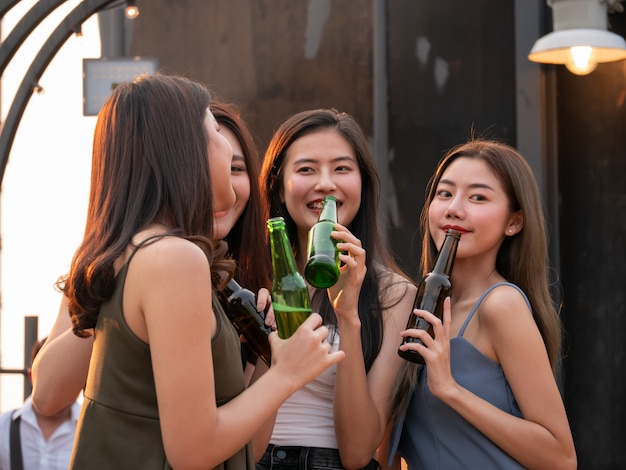 Group of asian friend cheering and drinking at terrace party. Young people enjoying and hanging out on rooftop at sunset