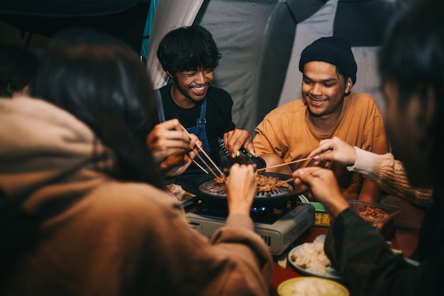 森でキャンプしながら夕食時に肉を焼くアジア人の友人のグループ