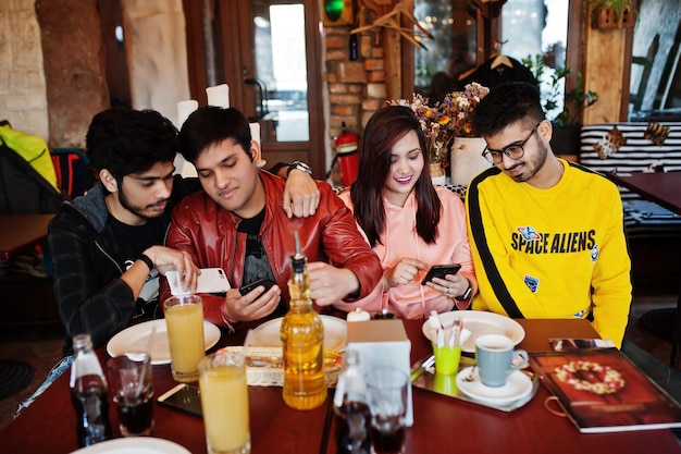카페에 앉아 있는 아시아 친구들 그룹 행복한 인도 사람들이 함께 소파에 앉아 휴대폰을 보면서 즐거운 시간을 보내고 있습니다.