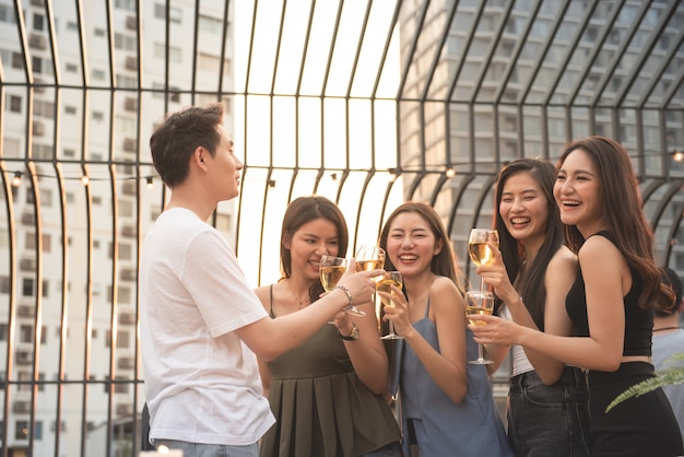 Il gruppo di genere multiplo asiatico che tiene il bicchiere di vino chiacchiera insieme agli amici mentre celebra il partito di ballo sul night-club all'aperto del tetto, stile di vita di svago di giovane concetto di godimento di amicizia.