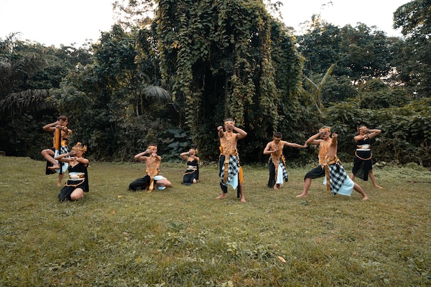 A Group of Asian people with golden dance costumes pose on the green grass in front of the jungle