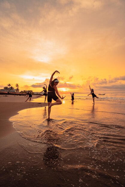 A group of Asian women is standing on the beach in black clothes and doing ballet moves in unison