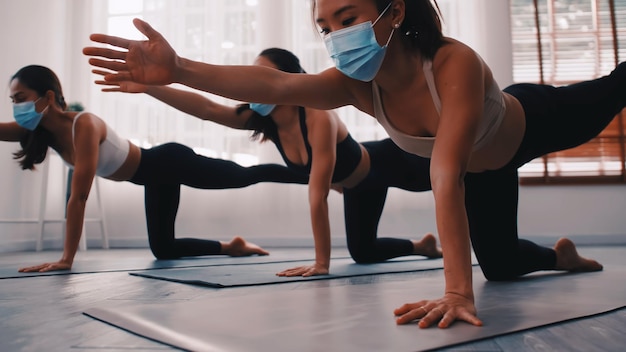 A group of Asian women wearing medical masks while doing yoga exercise at gym.