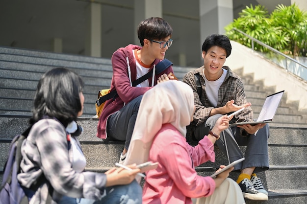 A group of Asiandiverse college students are relaxing on the stairs in front of the campus building