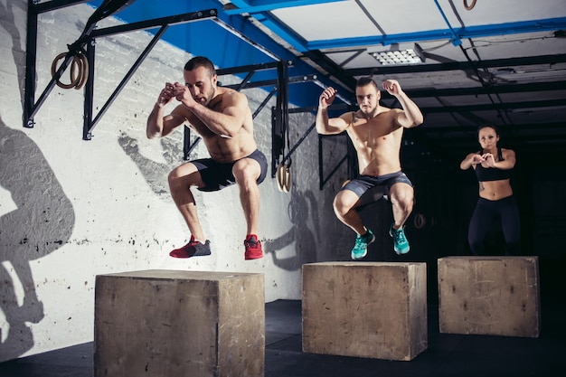 Group of athletic people jumpin over some boxes in a cross-training gym