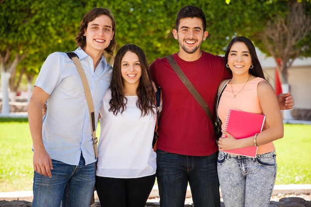 Group of attractive college friends with books and school bags hanging out at school and smiling