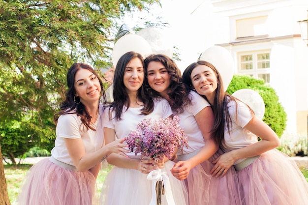 The group of beautiful girls clinging to the bride who is standing with a bouquet on the hen party