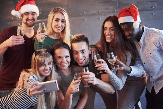 Group beautiful young people doing selfie in the new year party, best friends girls and boys together having fun, posing emotional lifestyle people. Hats santas and champagne glasses in their hands